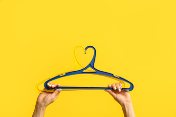 Female hands with clothes hangers on color background