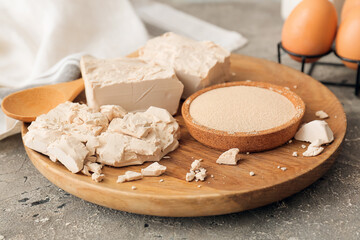 Wooden board with fresh and dry yeast on grunge background