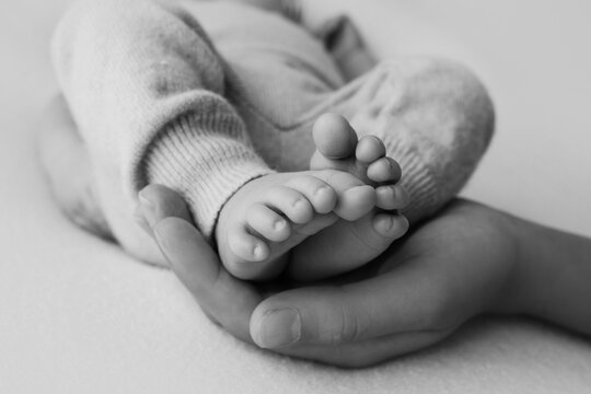 Female hands of young mother holding her newborn baby feet, closeup image with blur baby in background
