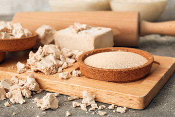 Wooden board with different yeast and rolling pin on grunge background