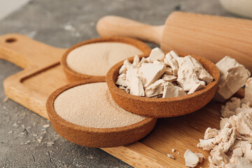 Wooden board with different yeast and rolling pin on grunge background