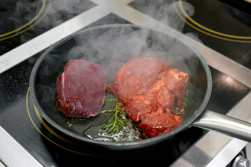 Raw beef and pork meat with rosemary cooking in a frying pan