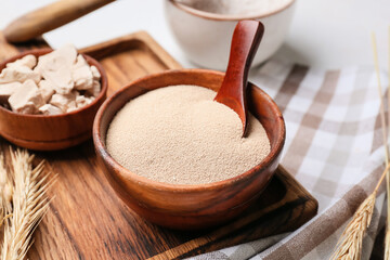 Wooden board with fresh and dry yeast on light background