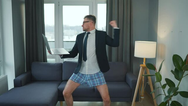 Caucasian man dressed in a jacket and underwear using laptop to make a video call from home in a modern apartment. Remote work during a pandemic