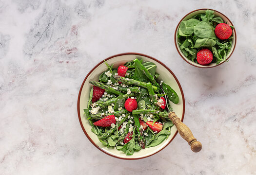 Fresh strawberry, green asparagus, feta cheese, baby spinach, and arugula salad served in a bowl