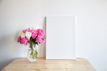Canvas mockup with pink flowers on wooden table on white wall background