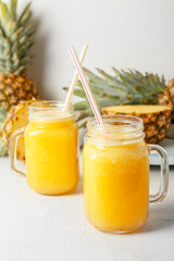 Mason jars of tasty pineapple smoothie on light background