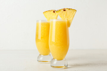 Glasses of tasty pineapple smoothie on light background