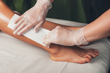 Close up photo of a caucasian spa worker having leg epilation procedures with a lying on the couch...