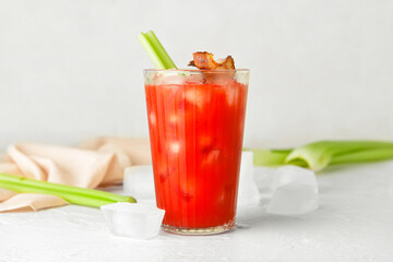 Glass of bloody mary cocktail garnished with bacon and celery on light background