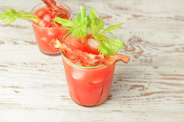 Glasses of bloody mary cocktail garnished with bacon and cilantro on light wooden background