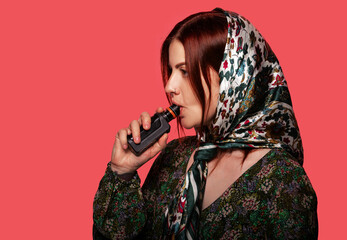 Woman smoking electronic cigarette with pierced nose and a fashionable headscarf. Red background,...