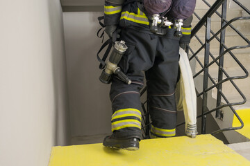 Naklejka premium a firefighter descends the stairs and carries a hose line and equipment for extinguishing fires indoors, front view