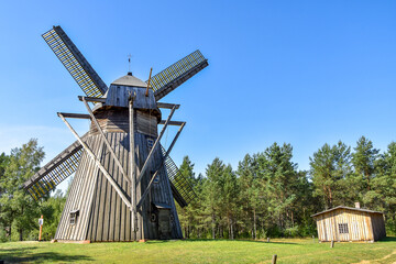 Old, wooden windmill from XIX century in a rural scenery with forest in the background