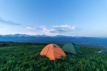 Two tents stand at the top of a green hill
