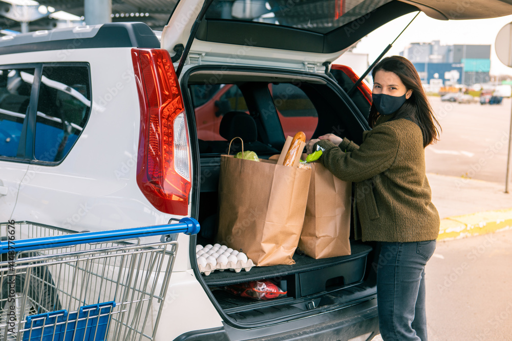 Wall mural woman put bags with products in car trunk after grocery store