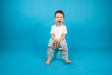 Full-length portrait of a yawning toddler sitting on a potty, blue background with copy space.