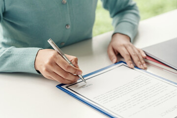 Close-up of a woman hand holding a pen about to sign contract documents at the office.