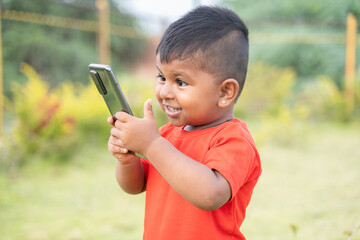 Portrait of Excited surprised Indian chubby kid Laughing by looking into mobile phone - Concept of...