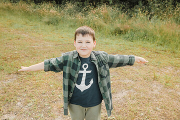 Little boy with an anchor on his t-shirt smiles happily and keeps arms wide open. Boy by the sea. Little child flies with his hands 