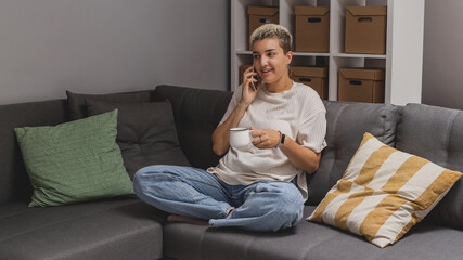 Obraz premium A woman lies on a sofa with a smartphone in a minimalistic home interior. High quality photo
