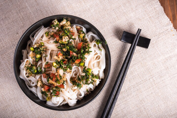 Bowl of rice noodles with spicy spicy asian homemade sauce on linen napkin with chopsticks, top view - vegan dish