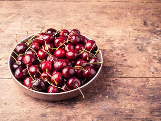 Bowl with ripe cherries on a wooden table, top view, copy space