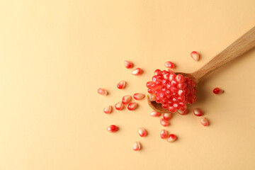 Wooden spoon with pomegranate seeds on beige background