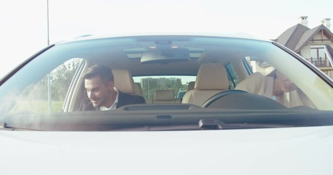 Front view of the caucasian husband and his wife sitting into the car and fastened with safety belts while preparing to the traveling. People and transport concept