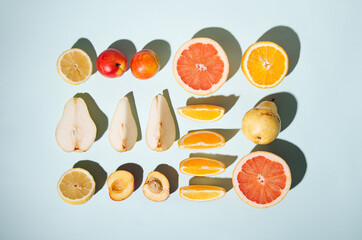 Neatly arranged fresh fruit on blue colored background. Minimal flat lay. Contrasting shadows.