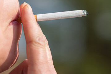 Middle age woman smoking cigarette outdoors with sun on her face. Closeup woman with cigarette in her mouth copy space.