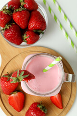 Glass jar of strawberry milkshake and ingredients on white background