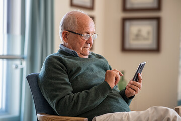 Senior man using smartphone at home - Powered by Adobe