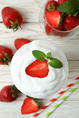 Glass of strawberry milkshake and ingredients on white wooden table