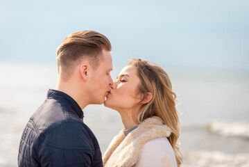 Naklejka premium Young couple kissing outdoor.Stunning outdoors portrait of young stylish fashion couple posing in spring sea background.
