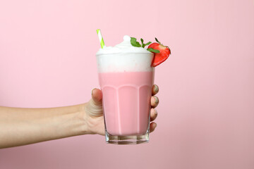 Female hand holds glass of strawberry milkshake on pink background