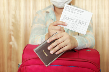 Obraz premium Woman in travel clothes wearing a medical mask showing covid-19 vaccination record card and passport and pink suitcase. Travel concept with vaccination.
