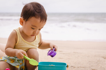 Asian boy child playing sand with his bucket on the beach in front of sea.