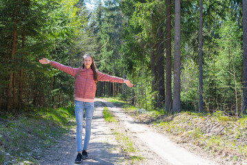Young traveler girl arms outstretched raised enjoying the fresh air in the green summer spring forest.Sunny day.