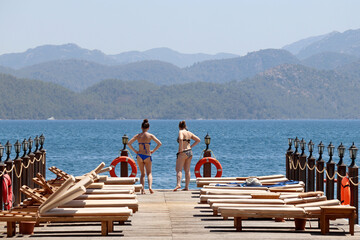 Sea resort, two girls in bikini sunbathing on a beach on green mountains background. Girlfriends...