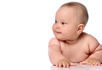 Focused infant child baby girl kid in diaper is lying on her stomach and watches aside attentively isolated on a white background