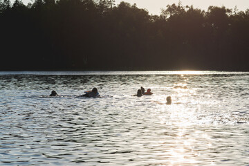 Silhouettes of people on a sunset lake background.Group of happy children having fun in summer lake or water.