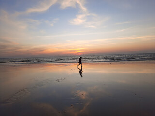 silhouette of a person on the beach, A calm and tranquil zen-like sunset at the beach with beautiful colours in blue and red with reflections on the water.