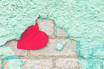 Valentine day background with red paper heart on a rustic green crumbling wall. heart is stuck on the stucco.