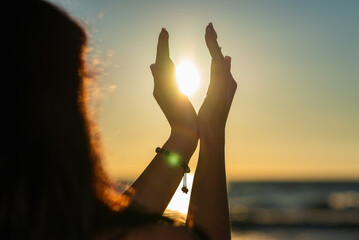 Silhouette of young woman's hands relaxing, happy meditating and holding sunset against golden hour sky on the beach.