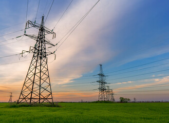 high voltage lines and power pylons in a green agricultural field against a saturated sunset sky