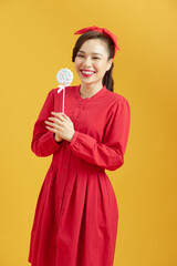 Laughing young woman holding lollipop over yellow background and looking at camera