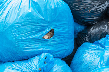 Torn blue trash bag with leaves sticking out of a hole