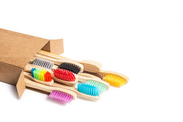 Cepillos de dientes de bambo de colores junto a una caja de cartón reciclable sobre un fondo...