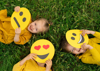 Three funny happy girls hide and look out from behind the faces of emoticons with different...